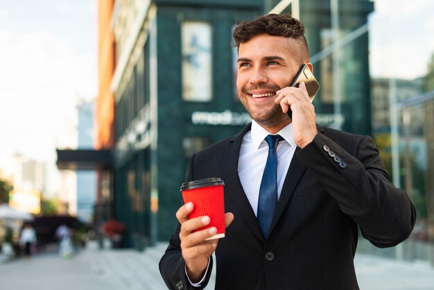 Uomo d'affari all'aperto che beve il suo caffè e parla al telefono