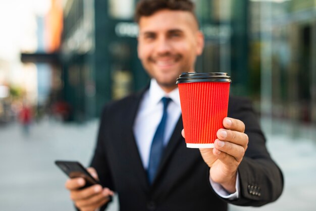 Uomo d'affari all'aperto che tiene una tazza di caffè rossa