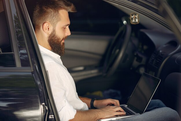 Uomo d'affari alla moda che si siede in un'automobile e usa il computer portatile