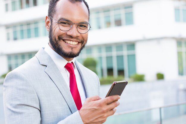 Uomo d'affari allegro felice con gli smartphones che posano all'aperto