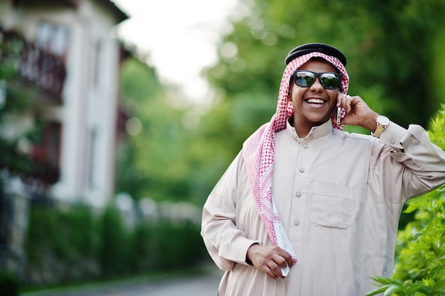 Uomo d'affari arabo mediorientale posato per strada con occhiali da sole che parla sul telefono cellulare
