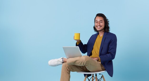 uomo d'affari asiatico sorridendo felice utilizzando il computer portatile seduto sulla sedia bianca e bevendo caffè