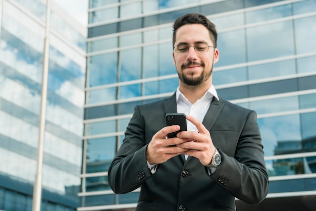 Uomo d&#39;affari bello che gode dell&#39;invio di messaggi di testo sul telefono cellulare