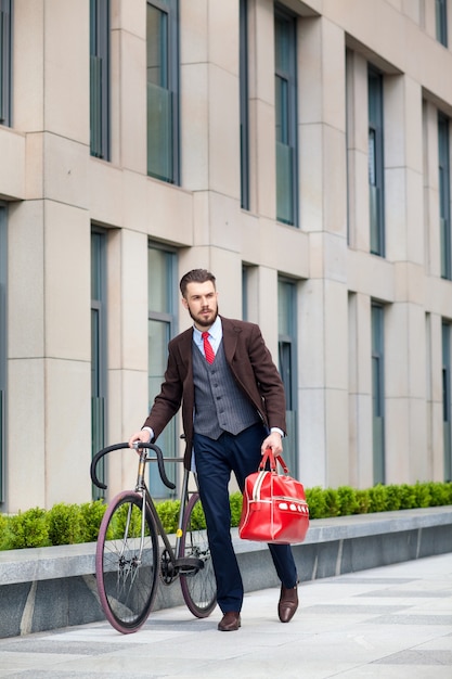 Uomo d'affari bello in una giacca e borsa rossa e la sua bicicletta per le strade della città.