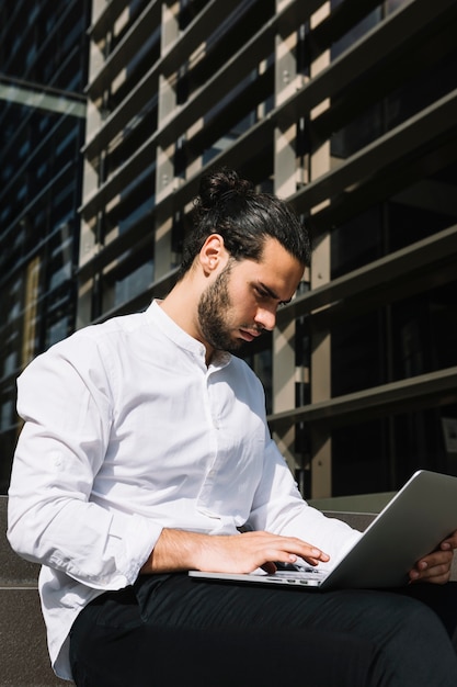 Uomo d&#39;affari bello serio che si siede fuori dell&#39;ufficio che scrive sul computer portatile