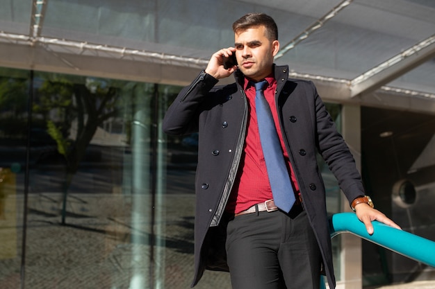 Uomo d&#39;affari bello serio in cappotto nero che parla sul telefono