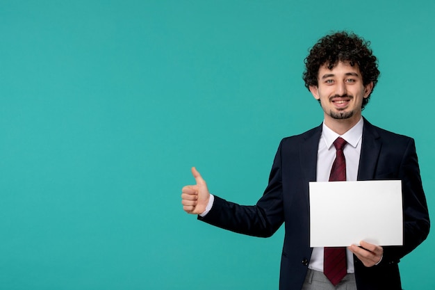 Uomo d'affari carino ragazzo carino in abito da ufficio nero che mostra un buon segno di gesto e tiene la carta