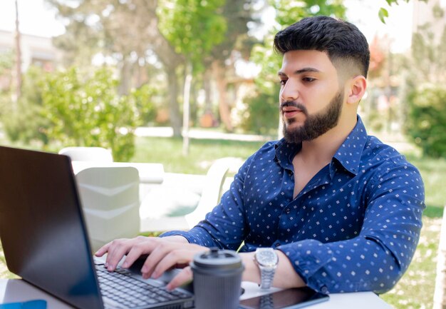Uomo d'affari caucasico bello che scrive sul computer portatile mentre è seduto all'aperto
