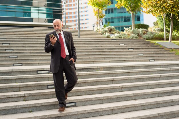 Uomo d'affari che cammina sui punti e che per mezzo dello smartphone