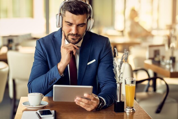 Uomo d'affari che indossa le cuffie durante la navigazione in rete sul touchpad in un bar