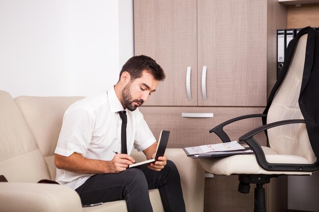 Uomo d'affari che lavora in ufficio sul divano mettendo lunghe ore di lavoro. Imprenditore in ambiente professionale