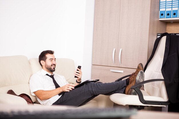 Uomo d'affari che lavora in ufficio sul divano mettendo lunghe ore di lavoro. Imprenditore in ambiente professionale