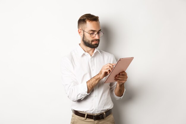 Uomo d'affari che lavora sulla tavoletta digitale, guardando occupato, in piedi