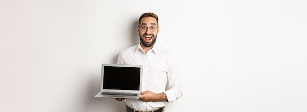 Uomo d'affari che mostra lo schermo del laptop che sembra eccitato in piedi su sfondo bianco
