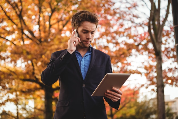 Uomo d'affari che parla sul telefono cellulare e che tiene compressa digitale