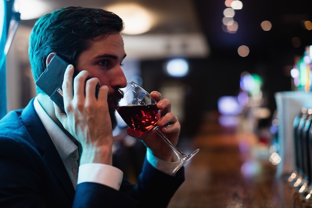Uomo d'affari che parla sul telefono cellulare mentre bevendo bicchiere di vino