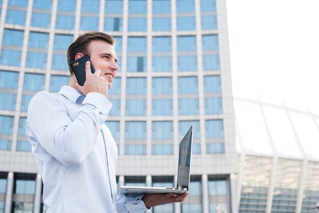 Uomo d'affari che parla sul telefono mentre tenendo computer portatile