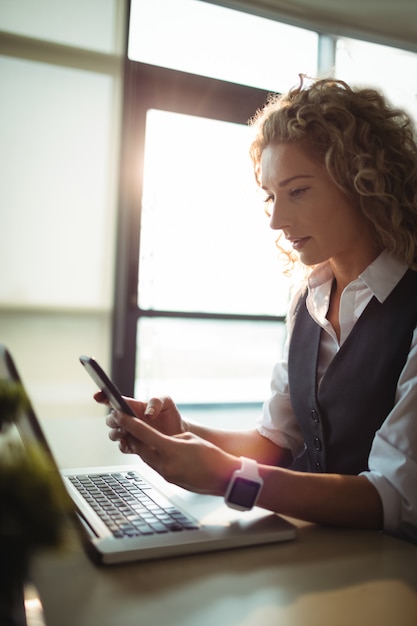 Uomo d'affari che per mezzo del telefono cellulare mentre lavorando al computer portatile