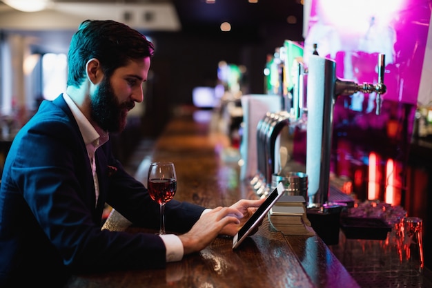 Uomo d'affari che per mezzo della compressa digitale con il vetro di vino sul contatore