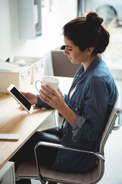 Uomo d'affari che per mezzo della compressa digitale mentre mangiando tazza di caffè