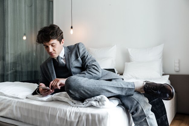Uomo d'affari che per mezzo dello smartphone mentre trovandosi su un letto