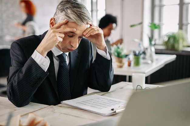 Uomo d'affari che si sente stressato durante la lettura di rapporti finanziari problematici in ufficio