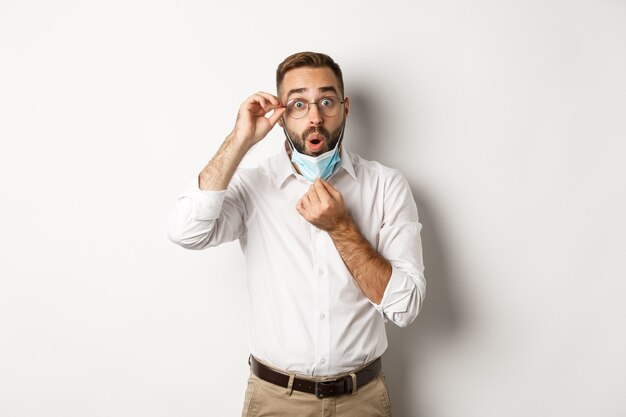 Uomo d'affari colpito decollare maschera medica, guardando sorpreso, in piedi