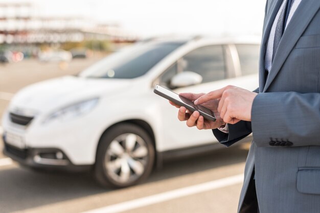 Uomo d&#39;affari con lo smartphone davanti alla macchina