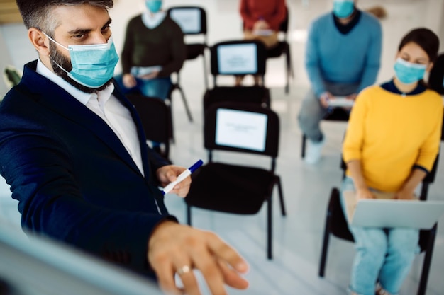 Uomo d'affari con maschera facciale che fa una presentazione sulla lavagna nella sala riunioni