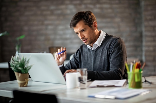 Uomo d'affari concentrato che passa attraverso il progetto con molta attenzione mentre lavora su un computer in ufficio