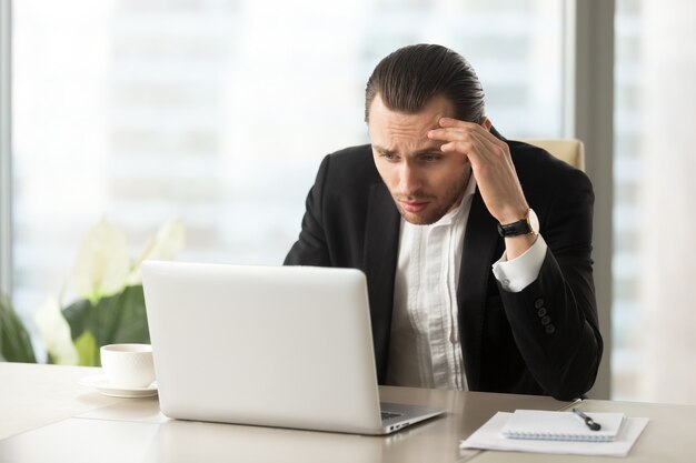 Uomo d&#39;affari confuso turbato che esamina lo schermo del computer portatile