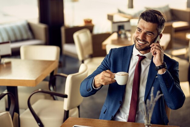 Uomo d'affari felice che beve caffè e parla al telefono in un bar