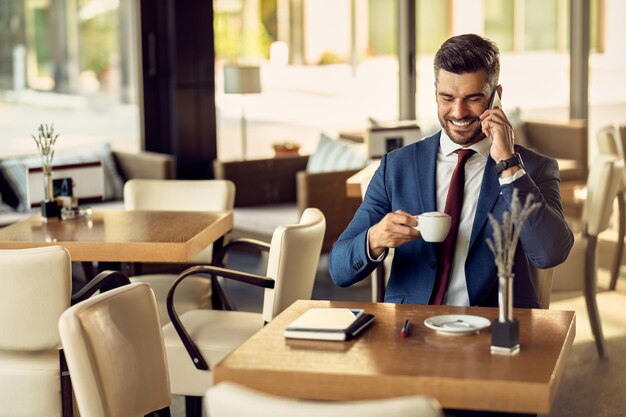 Uomo d'affari felice che fa una telefonata mentre si gode la pausa caffè in un caffè