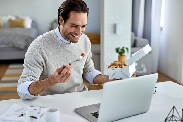 Uomo d'affari felice che naviga in rete sul laptop durante la pausa pranzo a casa