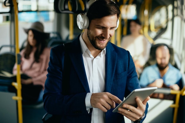 Uomo d'affari felice che naviga in rete sul touchpad mentre viaggia in autobus pubblico