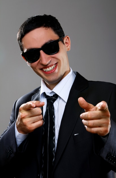 Uomo d'affari felice in occhiali da sole che indica voi