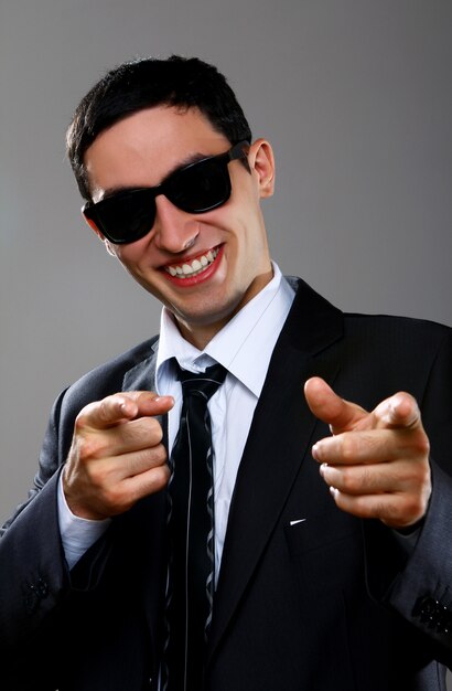 Uomo d'affari felice in occhiali da sole che indica voi