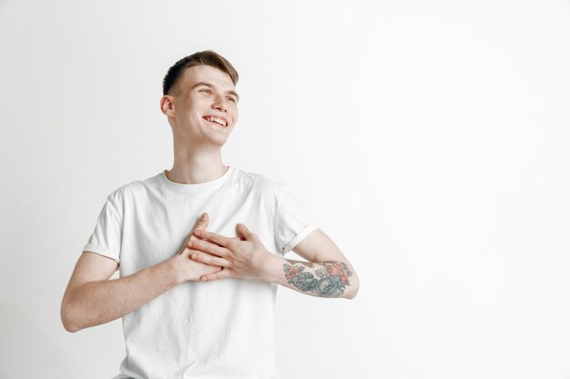 Uomo d'affari felice in piedi, sorridente isolato su sfondo grigio studio. Bellissimo ritratto maschile a mezzo busto. I giovani soddisfano l'uomo. Emozioni umane, concetto di espressione facciale.