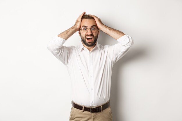 Uomo d'affari frustrato che tiene le mani sulla testa, guardando scioccato e ansioso, in piedi