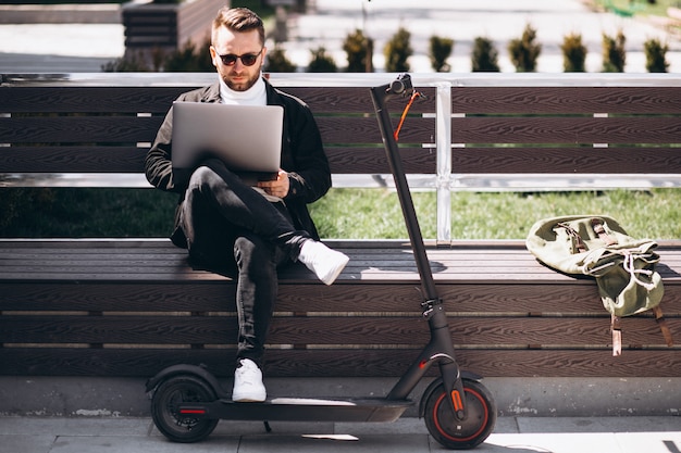 Uomo d'affari giovane seduto sulla panchina e lavorando sul computer