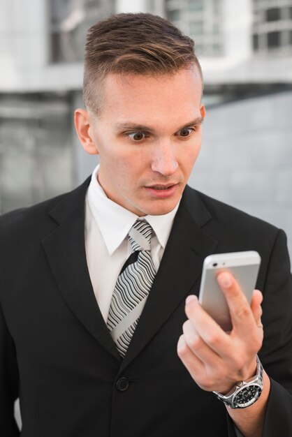 Uomo d&#39;affari guardando smartphone con espressione sorpresa