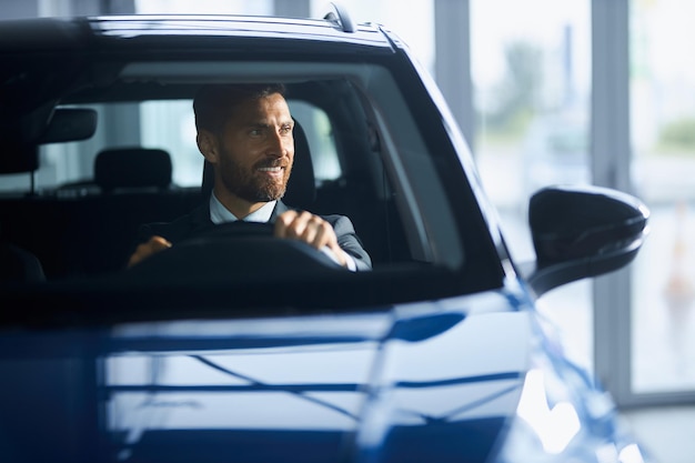 Uomo d'affari in giacca e cravatta che compra un'auto nuova al salone moderno