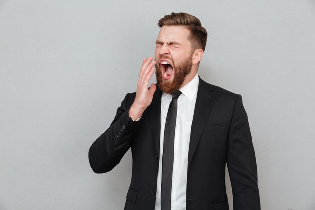 Uomo d'affari in tuta che sbadiglia e che copre la bocca con la mano