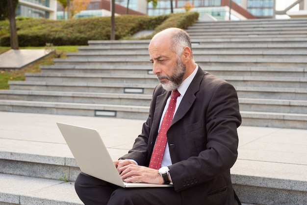 Uomo d'affari maturo serio che utilizza computer portatile nella via