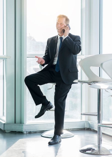 Uomo d&#39;affari maturo sorridente che parla sullo smartphone in ufficio