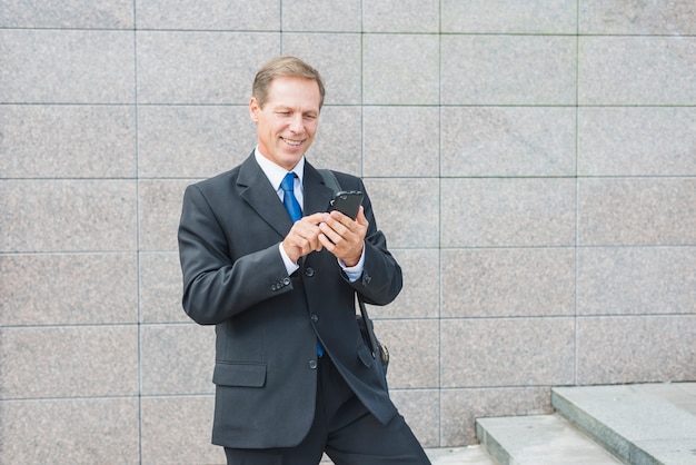 Uomo d&#39;affari maturo sorridente che per mezzo del telefono cellulare all&#39;aperto