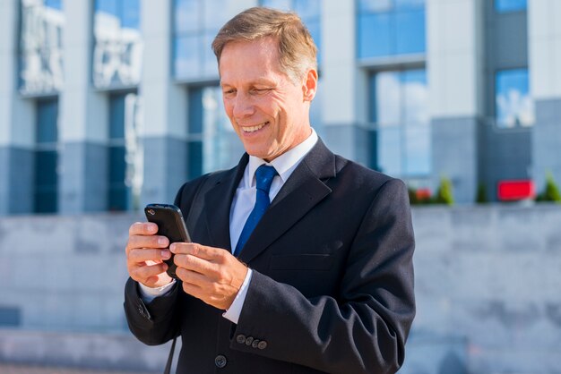 Uomo d&#39;affari maturo sorridente che per mezzo dello smartphone