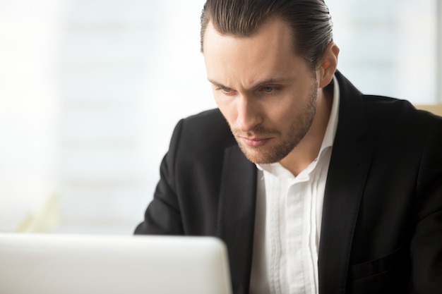 Uomo d&#39;affari messo a fuoco che considera lo schermo del computer portatile