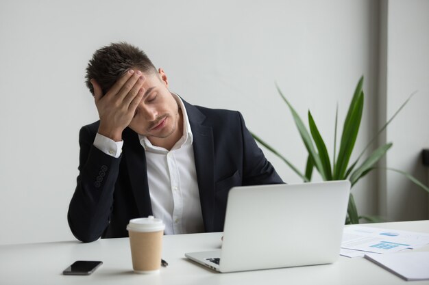 Uomo d&#39;affari millenario frustrato che ha forte emicrania stanco dal lavoro del computer portatile