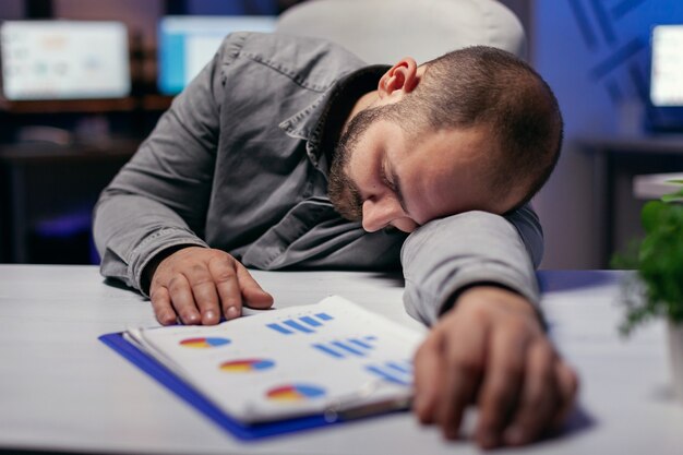 Uomo d'affari oberato di lavoro che riposa la testa sul tablet. Dipendente maniaco del lavoro che si addormenta a causa di mentre lavora a tarda notte da solo in ufficio per un importante progetto aziendale.